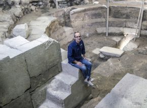 הארכיאולוג ג'ו עוזיאל מיושב על מדרגות המבנה דמוי התיאטרון בחפירת קשת וילסון