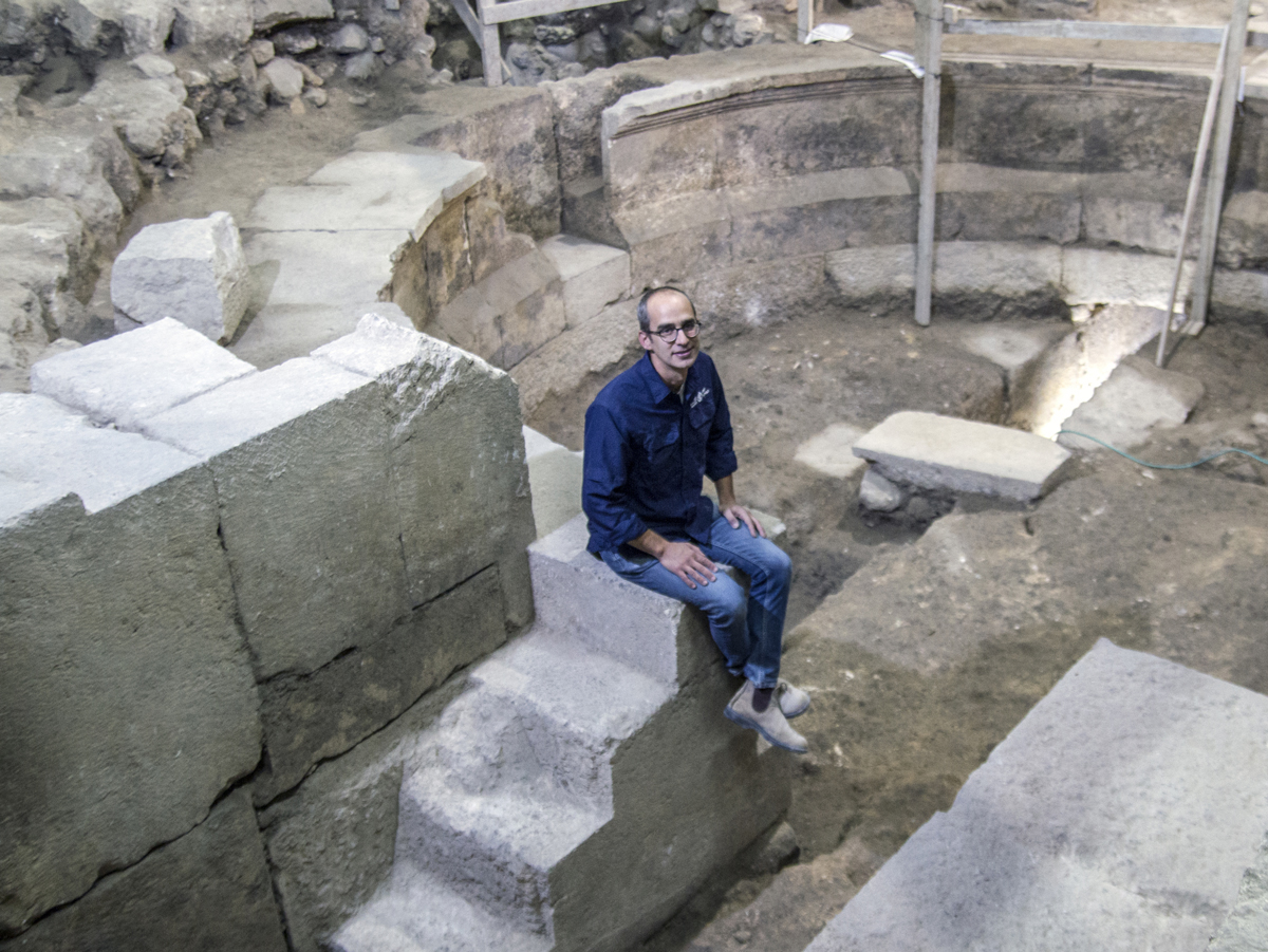הארכיאולוג ג'ו עוזיאל מיושב על מדרגות המבנה דמוי התיאטרון בחפירת קשת וילסון
